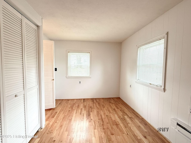 unfurnished bedroom featuring light wood finished floors, baseboard heating, and a closet