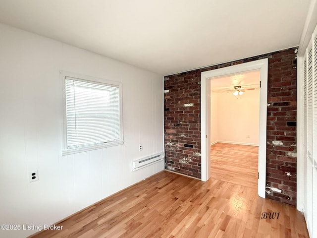 unfurnished room featuring brick wall, baseboard heating, and light wood-type flooring