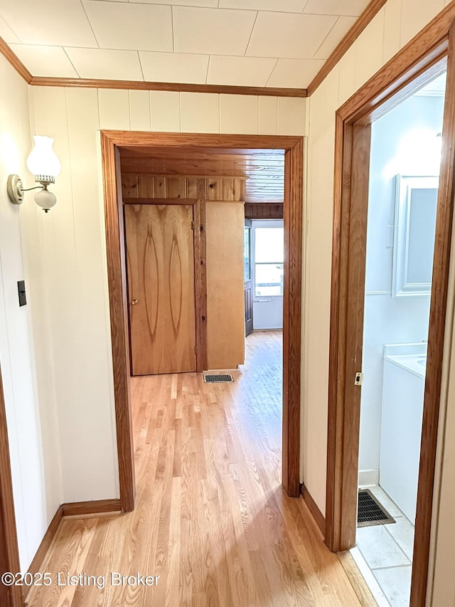 corridor with light wood-type flooring, baseboards, visible vents, and crown molding