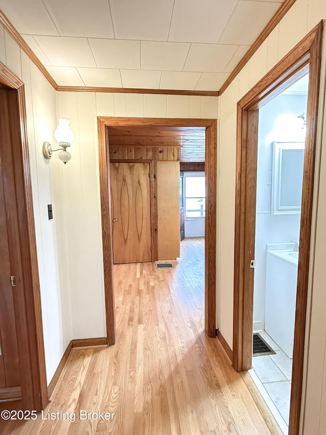 hall featuring light wood finished floors, baseboards, and crown molding