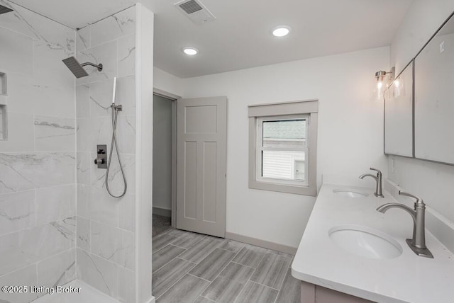 full bath featuring double vanity, visible vents, a tile shower, and a sink