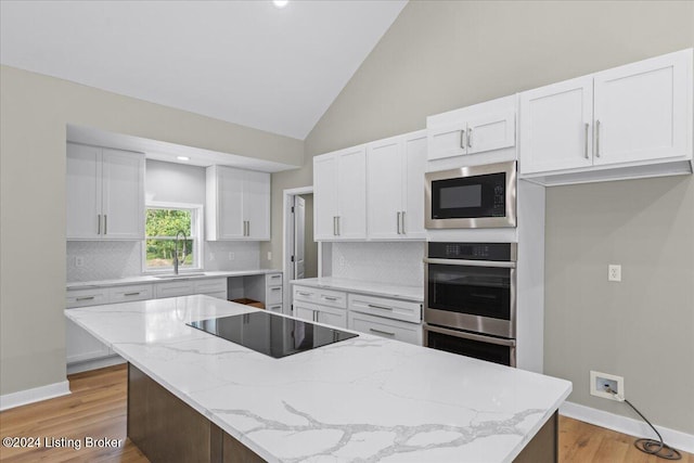 kitchen featuring black electric stovetop, stainless steel double oven, built in microwave, white cabinetry, and a center island