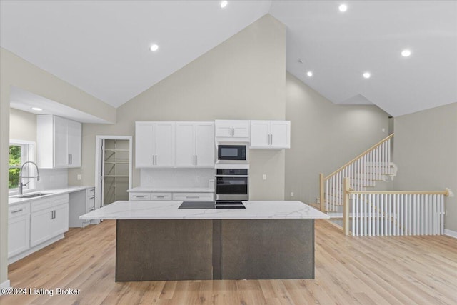 kitchen featuring light wood finished floors, white cabinets, a center island, black appliances, and a sink