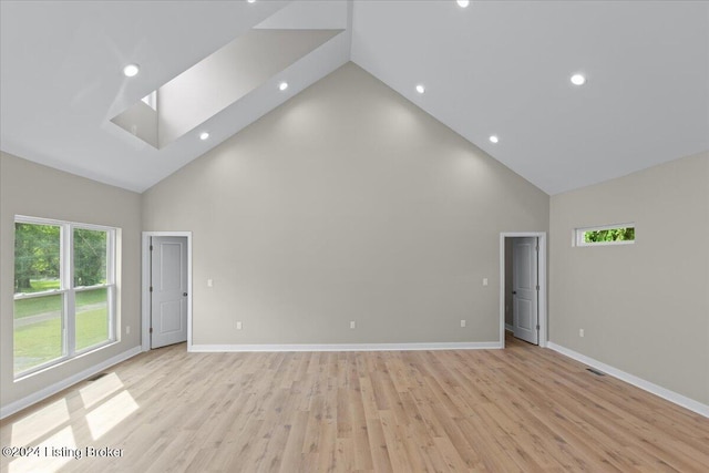 unfurnished room with high vaulted ceiling, light wood finished floors, a skylight, and baseboards