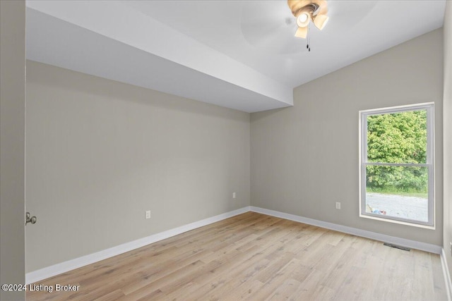 empty room with visible vents, vaulted ceiling, ceiling fan, light wood-type flooring, and baseboards