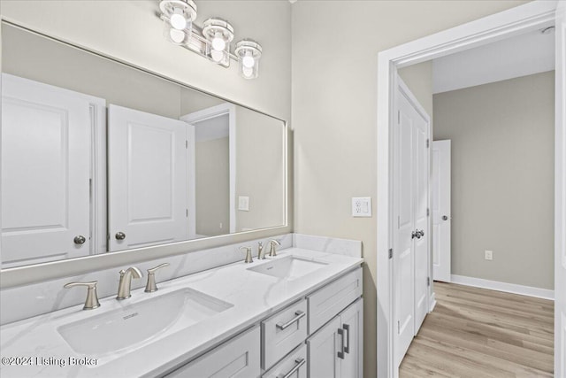 bathroom featuring double vanity, wood finished floors, a sink, and baseboards