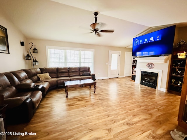 living room featuring wood finished floors, baseboards, a ceiling fan, lofted ceiling, and a fireplace