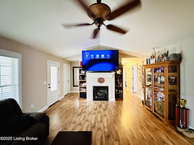 living area with baseboards, lofted ceiling, a fireplace, wood finished floors, and a ceiling fan