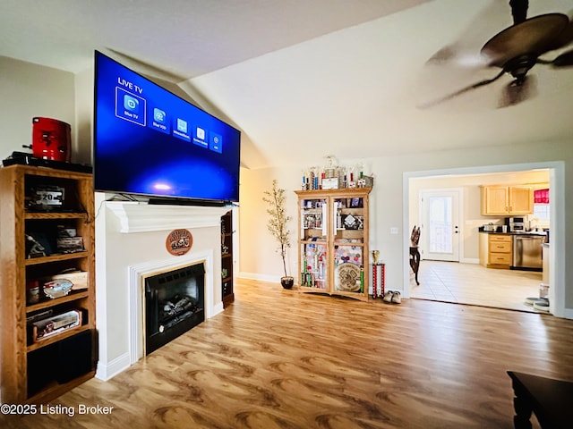 living room featuring a ceiling fan, wood finished floors, a fireplace, and vaulted ceiling