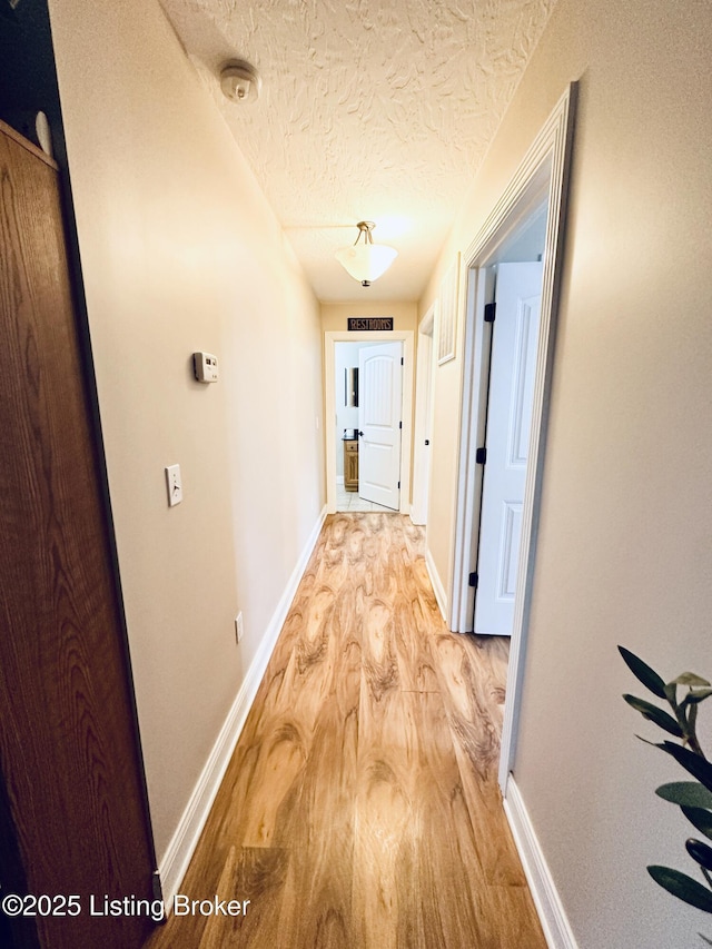 hallway with a textured ceiling, light wood-type flooring, and baseboards