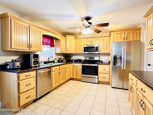 kitchen with dark countertops, ceiling fan, light brown cabinetry, appliances with stainless steel finishes, and a sink