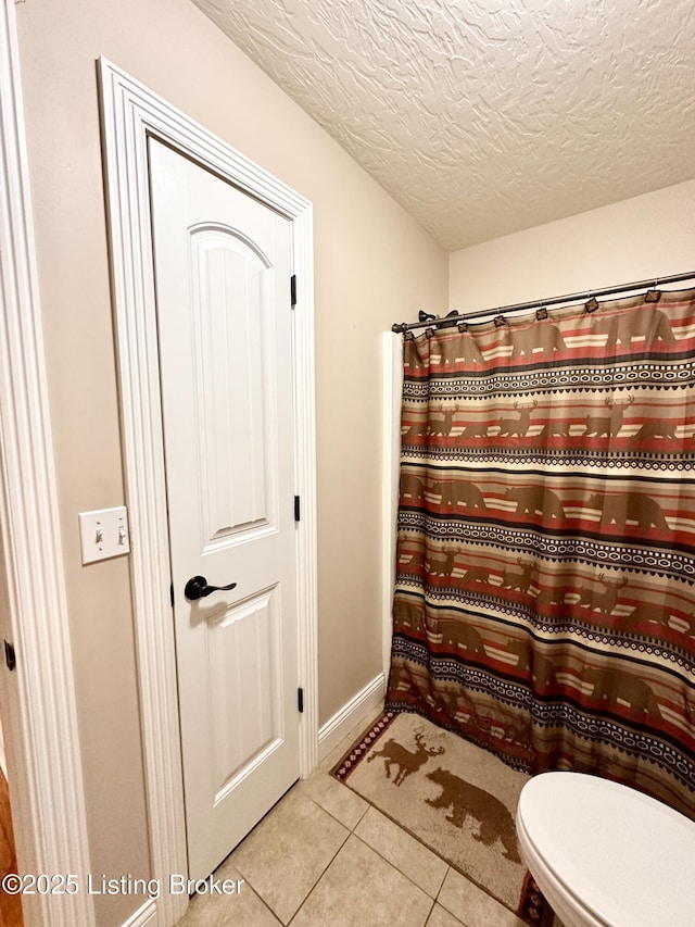 full bath featuring tile patterned flooring, baseboards, toilet, a shower with shower curtain, and a textured ceiling