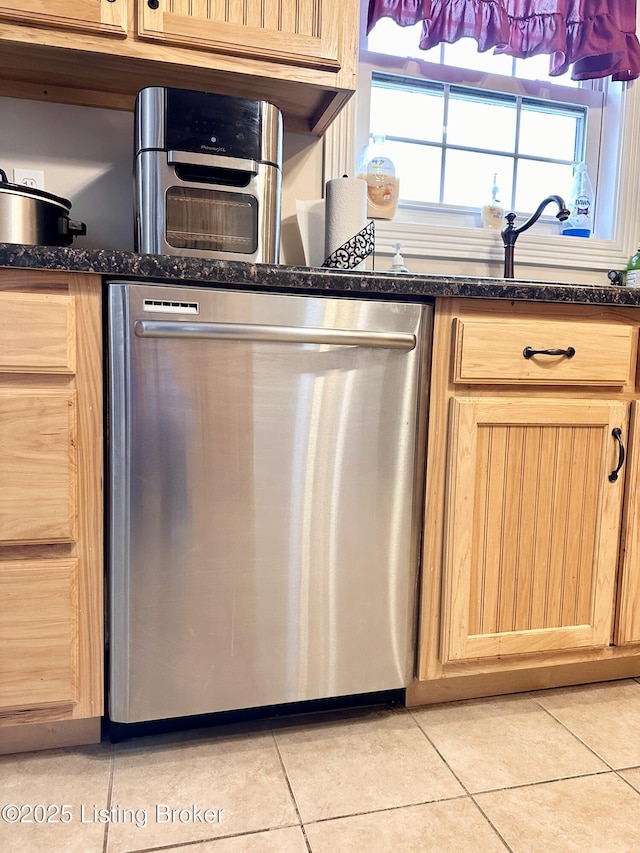 kitchen featuring dark stone counters, stainless steel dishwasher, light tile patterned flooring, and light brown cabinets