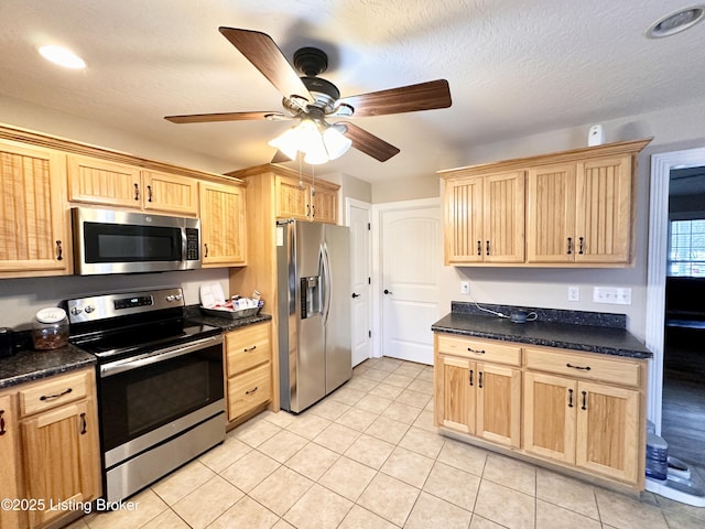 kitchen featuring dark countertops, light brown cabinets, light tile patterned floors, appliances with stainless steel finishes, and a textured ceiling