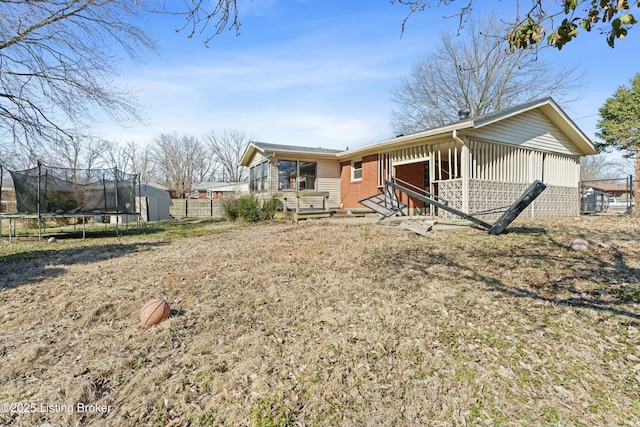 rear view of property featuring a trampoline, an outbuilding, brick siding, and fence