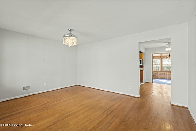 unfurnished room with ceiling fan with notable chandelier, visible vents, baseboards, and wood finished floors