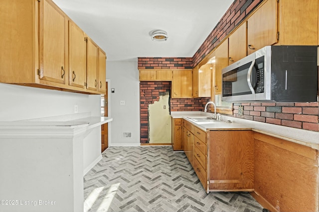 kitchen featuring light countertops, stainless steel microwave, a sink, and baseboards