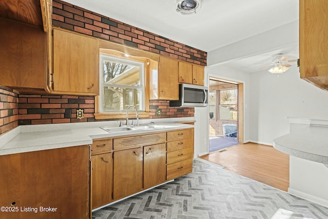 kitchen featuring tasteful backsplash, ceiling fan, stainless steel microwave, light countertops, and a sink