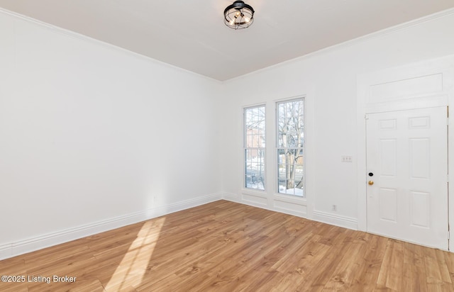 spare room featuring light wood finished floors, baseboards, and crown molding