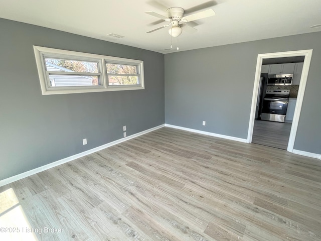 unfurnished room with ceiling fan, wood finished floors, visible vents, and baseboards