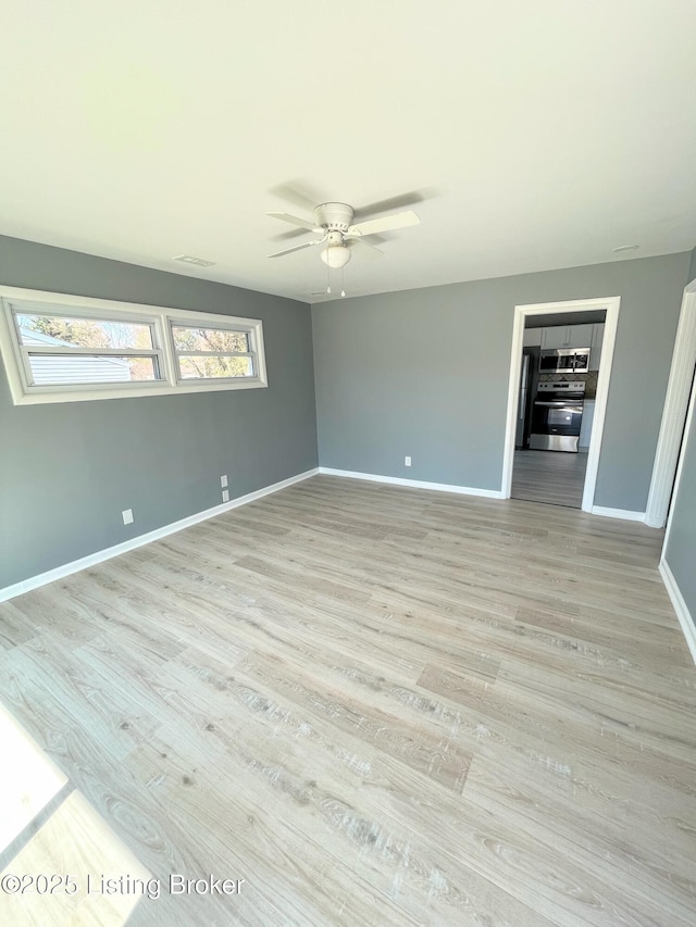 interior space with a ceiling fan, visible vents, light wood-style flooring, and baseboards