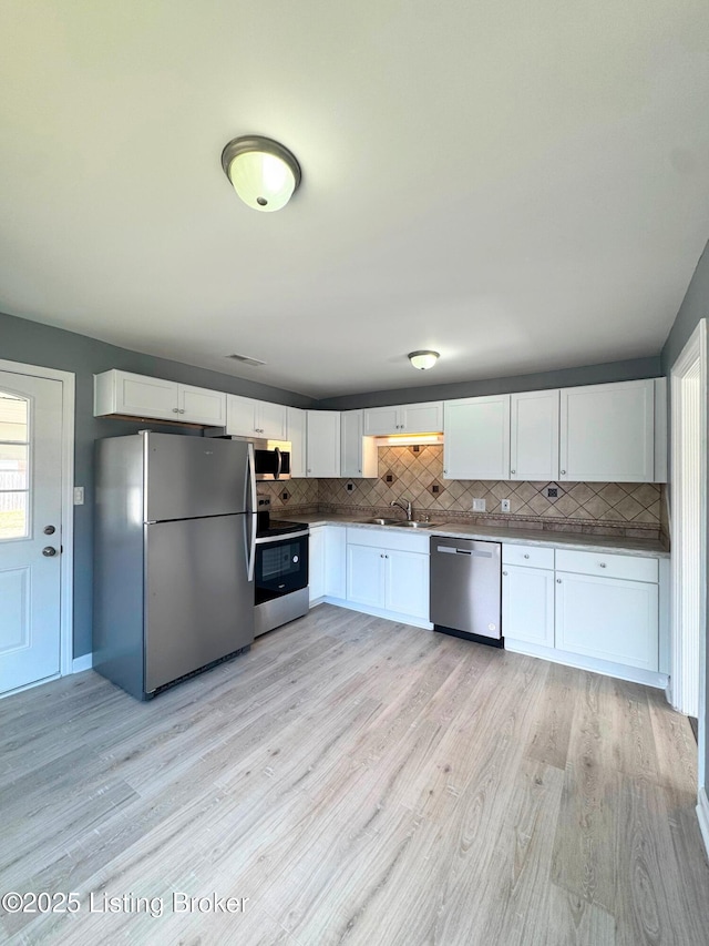 kitchen with tasteful backsplash, white cabinets, stainless steel appliances, light wood-style floors, and a sink