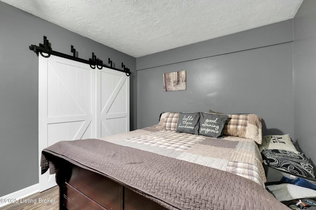 bedroom featuring a barn door, a textured ceiling, baseboards, and wood finished floors