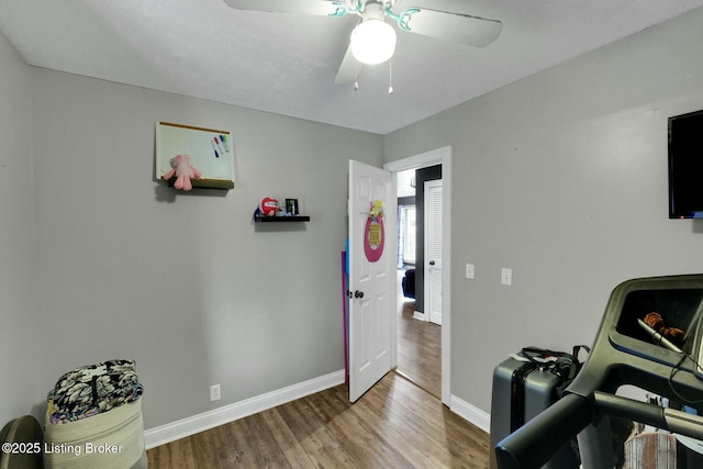 workout room with wood finished floors, a ceiling fan, and baseboards