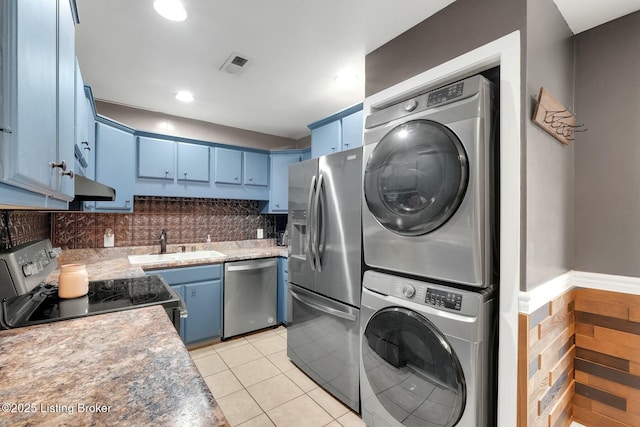 kitchen featuring light tile patterned floors, stainless steel appliances, stacked washer / drying machine, a sink, and blue cabinets