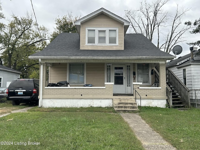 bungalow-style home with covered porch, brick siding, a front yard, and a shingled roof