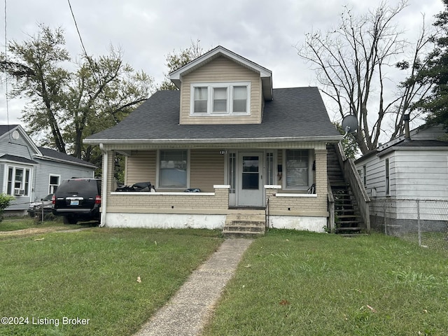 bungalow with a front yard, covered porch, brick siding, and roof with shingles