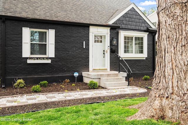entrance to property featuring brick siding and roof with shingles