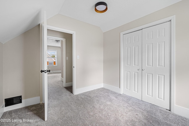 unfurnished bedroom with carpet, a closet, vaulted ceiling, visible vents, and baseboards
