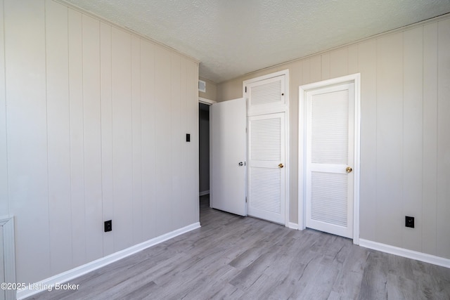 unfurnished bedroom with visible vents, a textured ceiling, baseboards, and wood finished floors