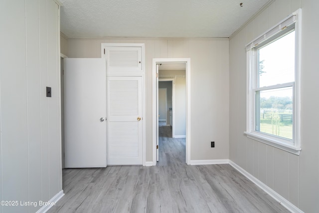 empty room featuring a textured ceiling, light wood finished floors, a wealth of natural light, and baseboards