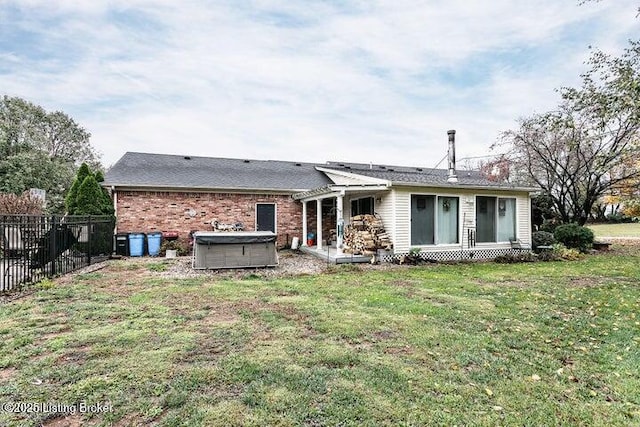 back of property with brick siding, fence, a hot tub, and a lawn