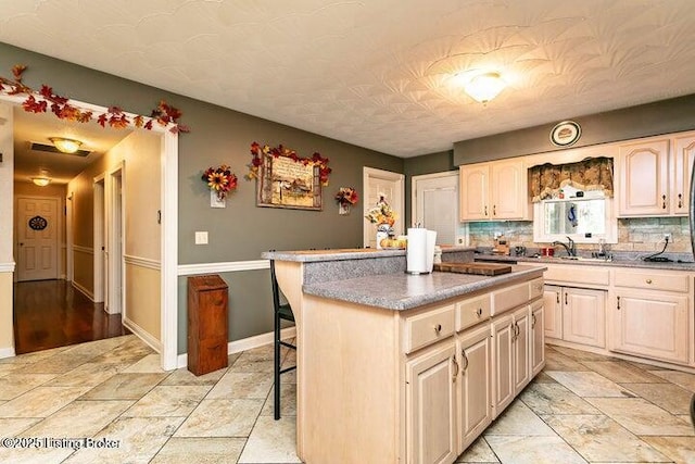 kitchen with baseboards, a kitchen island, a breakfast bar, backsplash, and a sink