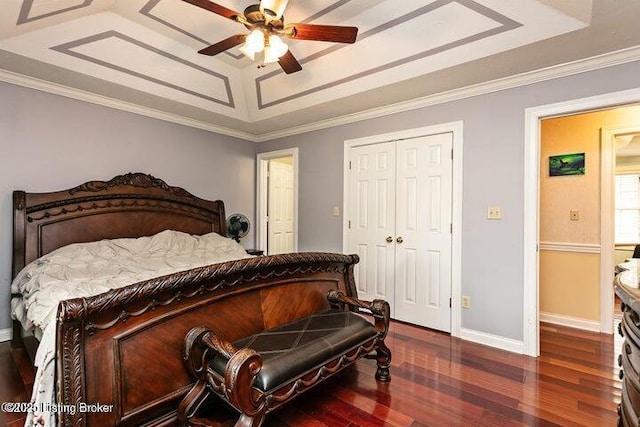 bedroom featuring baseboards, ornamental molding, wood finished floors, a tray ceiling, and a closet