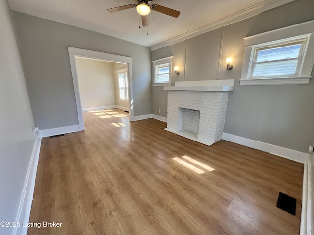 unfurnished living room featuring light wood-style floors, a brick fireplace, baseboards, and a ceiling fan