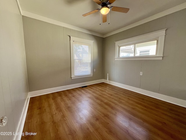 empty room with visible vents, wood finished floors, a ceiling fan, and baseboards