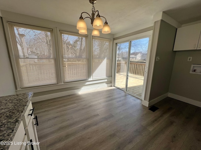 unfurnished dining area featuring a chandelier, dark wood-type flooring, and baseboards