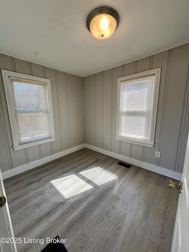 spare room featuring a wealth of natural light, a decorative wall, and wood finished floors