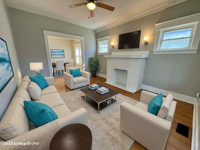 living area with light wood-style flooring, a fireplace, baseboards, and ceiling fan