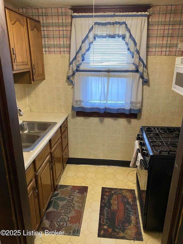 kitchen featuring light countertops, a sink, black gas range, and wallpapered walls