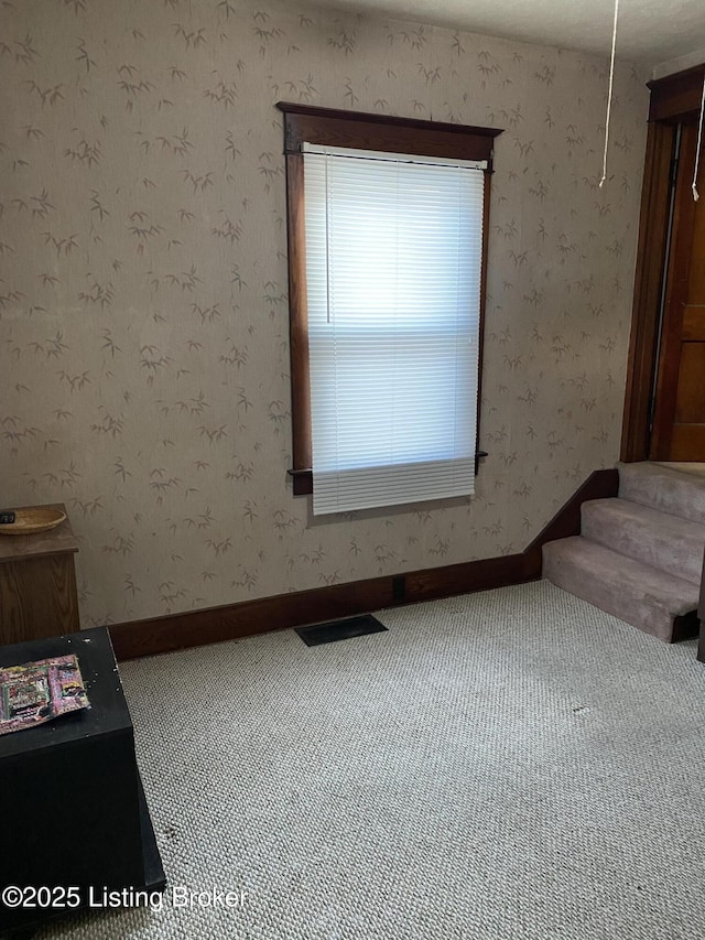 carpeted spare room featuring wallpapered walls, baseboards, stairway, and visible vents