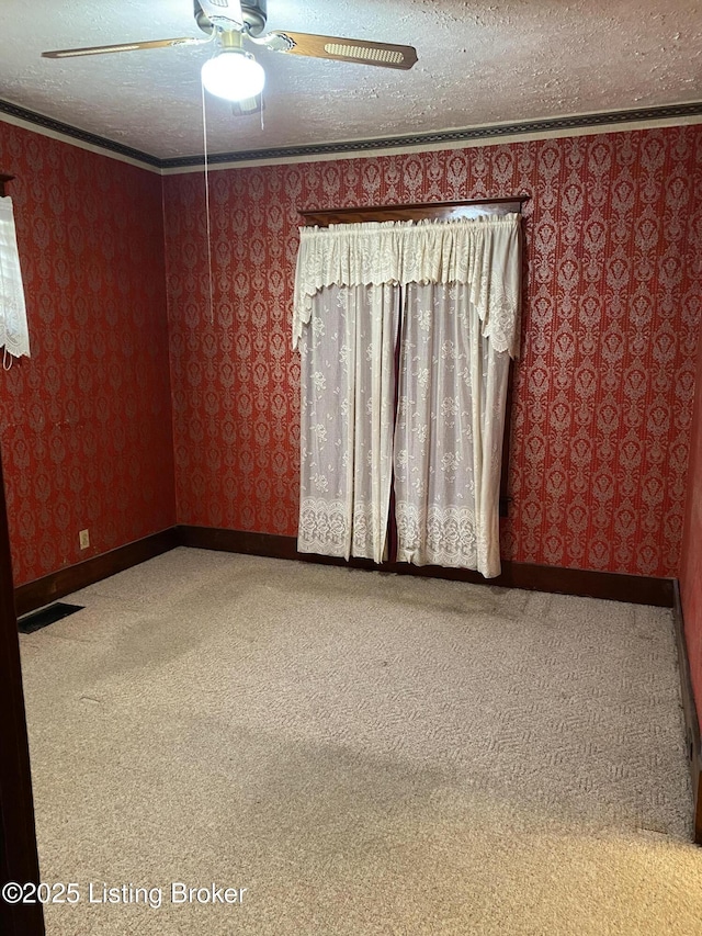 empty room with wallpapered walls, crown molding, a textured ceiling, and carpet flooring