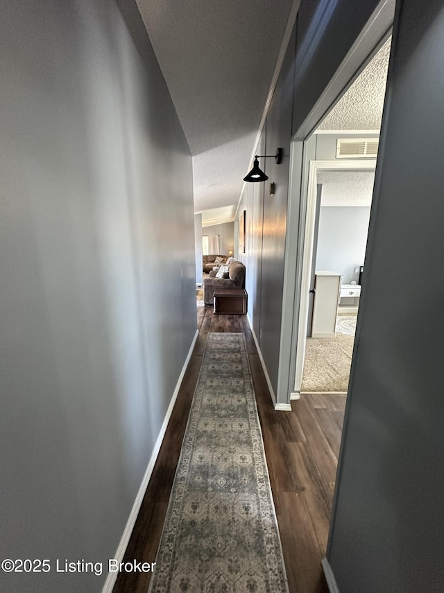 hall featuring visible vents, a textured ceiling, baseboards, and wood finished floors