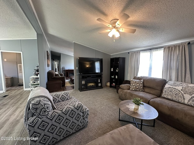 living room featuring a glass covered fireplace, lofted ceiling, ceiling fan, ornamental molding, and a textured ceiling