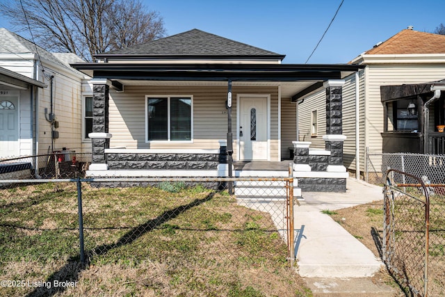 view of front of house with a fenced front yard, covered porch, a shingled roof, and a gate