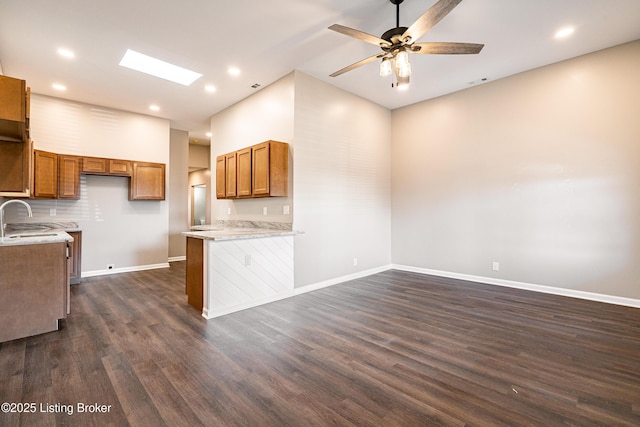 kitchen with dark wood-type flooring, a skylight, brown cabinetry, and baseboards